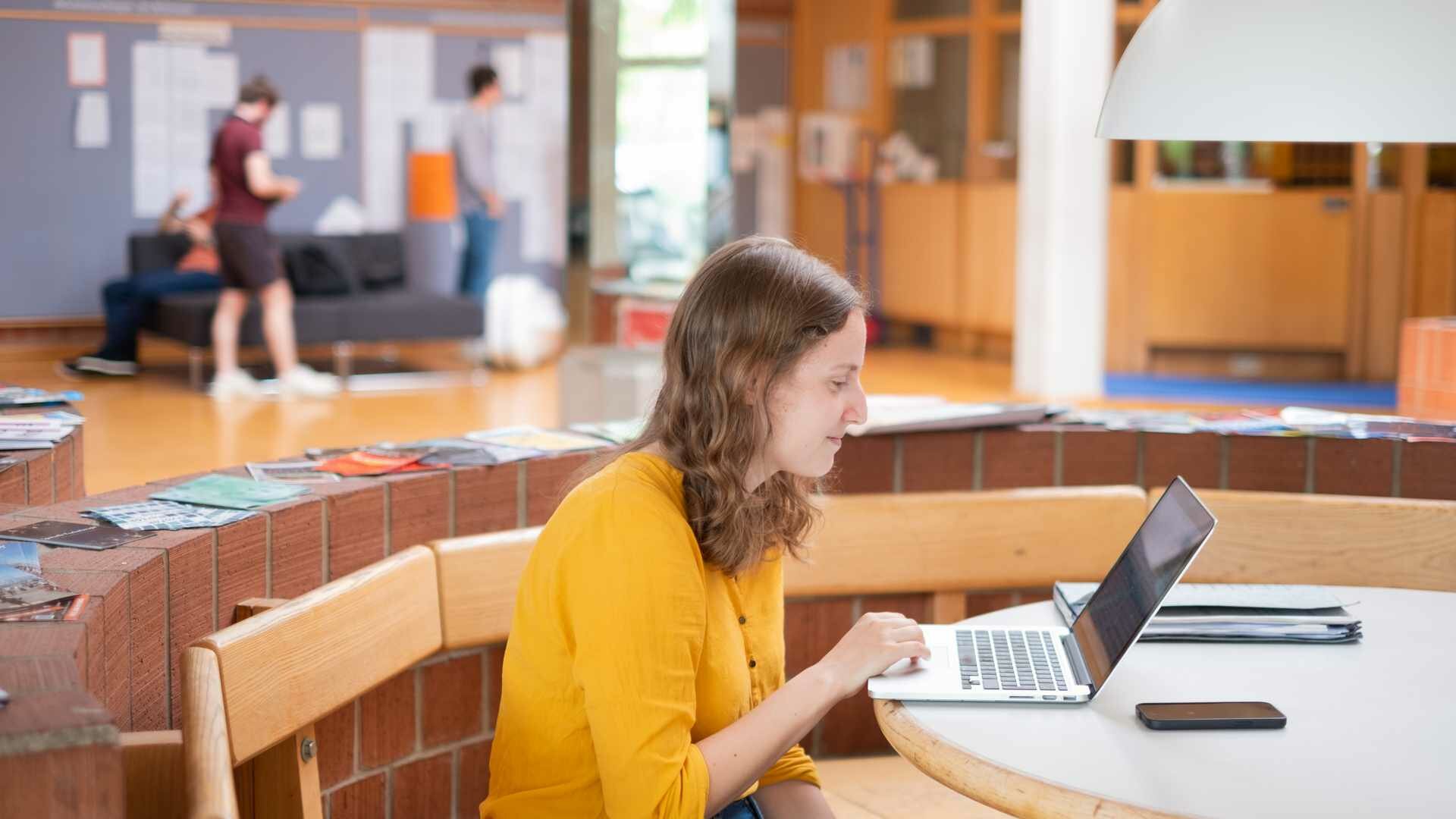 Studentin sitzt im Foyer der Hochschule an ihrem Laptop