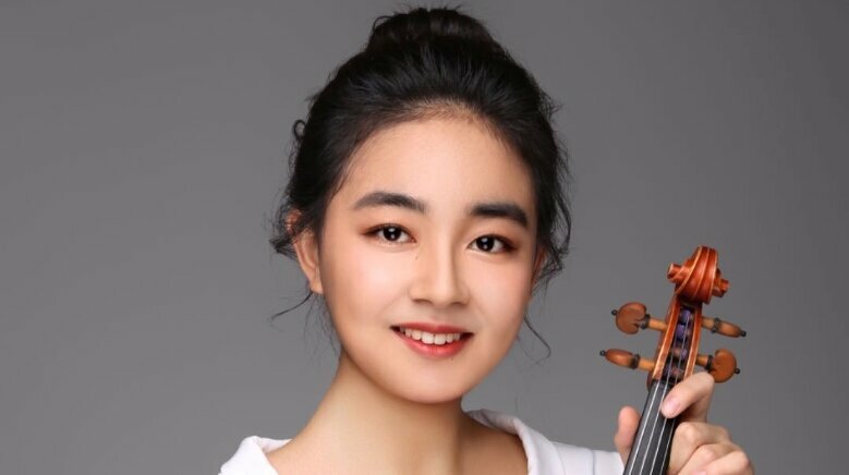 Yang Li mit Geige in der Hand vor einem grauen Hintergrund