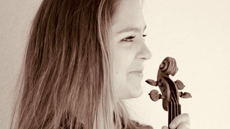 Eva Schall mit Geige in der Hand vor einem weiß-beigen Hintergrund