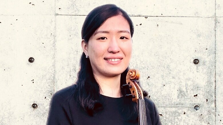 Saki Shimomiya steht mit Violine in der Hand vor einer Wand