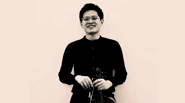 Cheng Yang Lai steht mit seiner Violine vor einem beigen Hintergrund