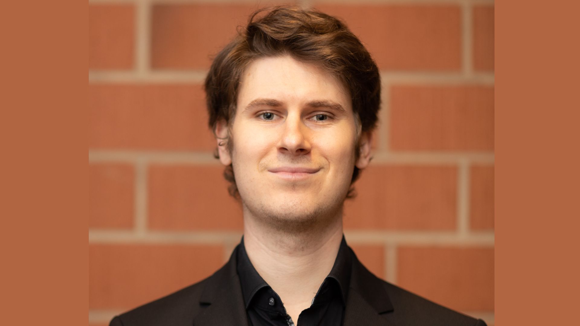 Benedikt Heisinger steht in einem schwarzen Anzug vor einer Backsteinwand der Hochschule für Musik Freiburg