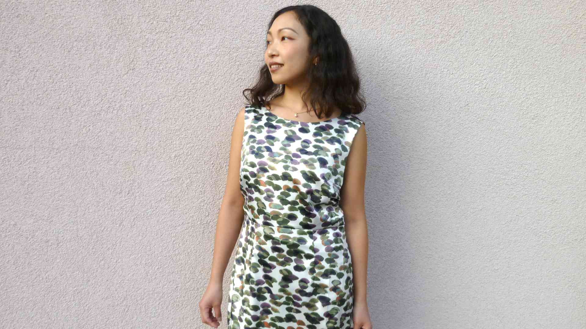 Tomoyo Inoue steht in einem weiß-grünen Kleid vor einer grauen Wand