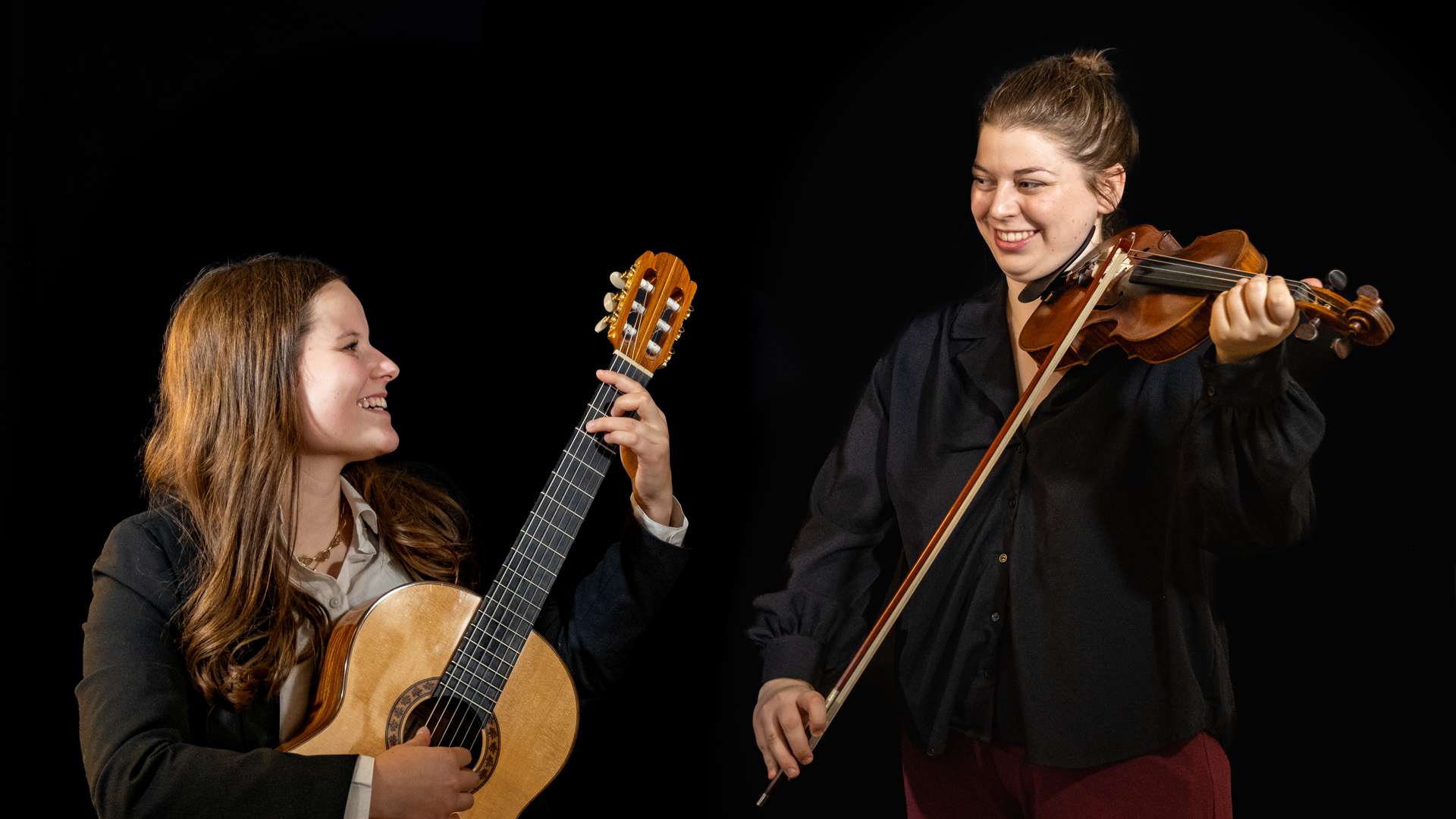 Chiara Wetzel sitzt links mit Gitarre in der Hand, Ambre Palusci steht mit Geige in der Hand neben ihr