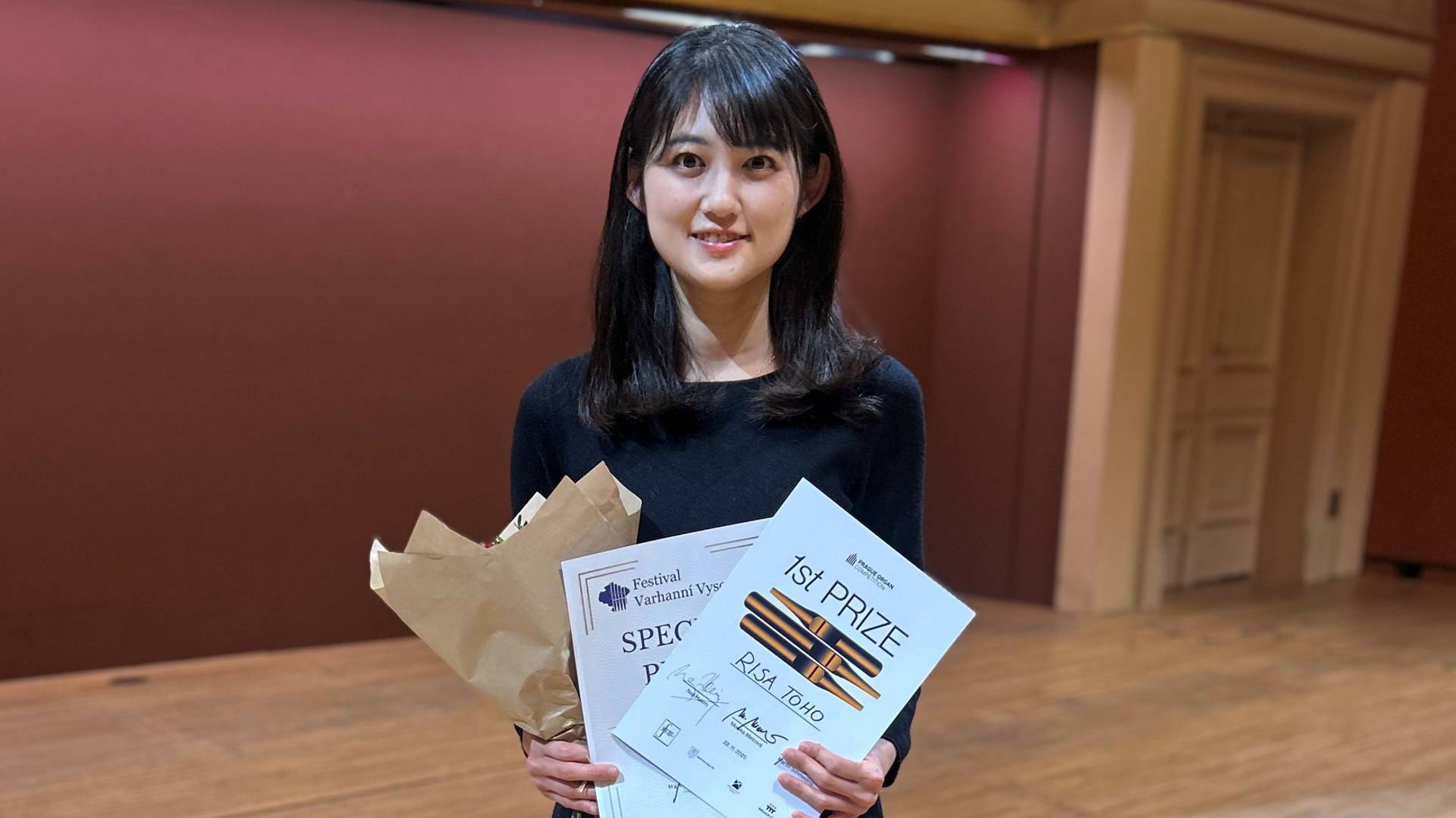 Risa Toho steht in einem Konzertsaal, in der Hand hält sie zwei Urkunden und einen Blumenstrauß