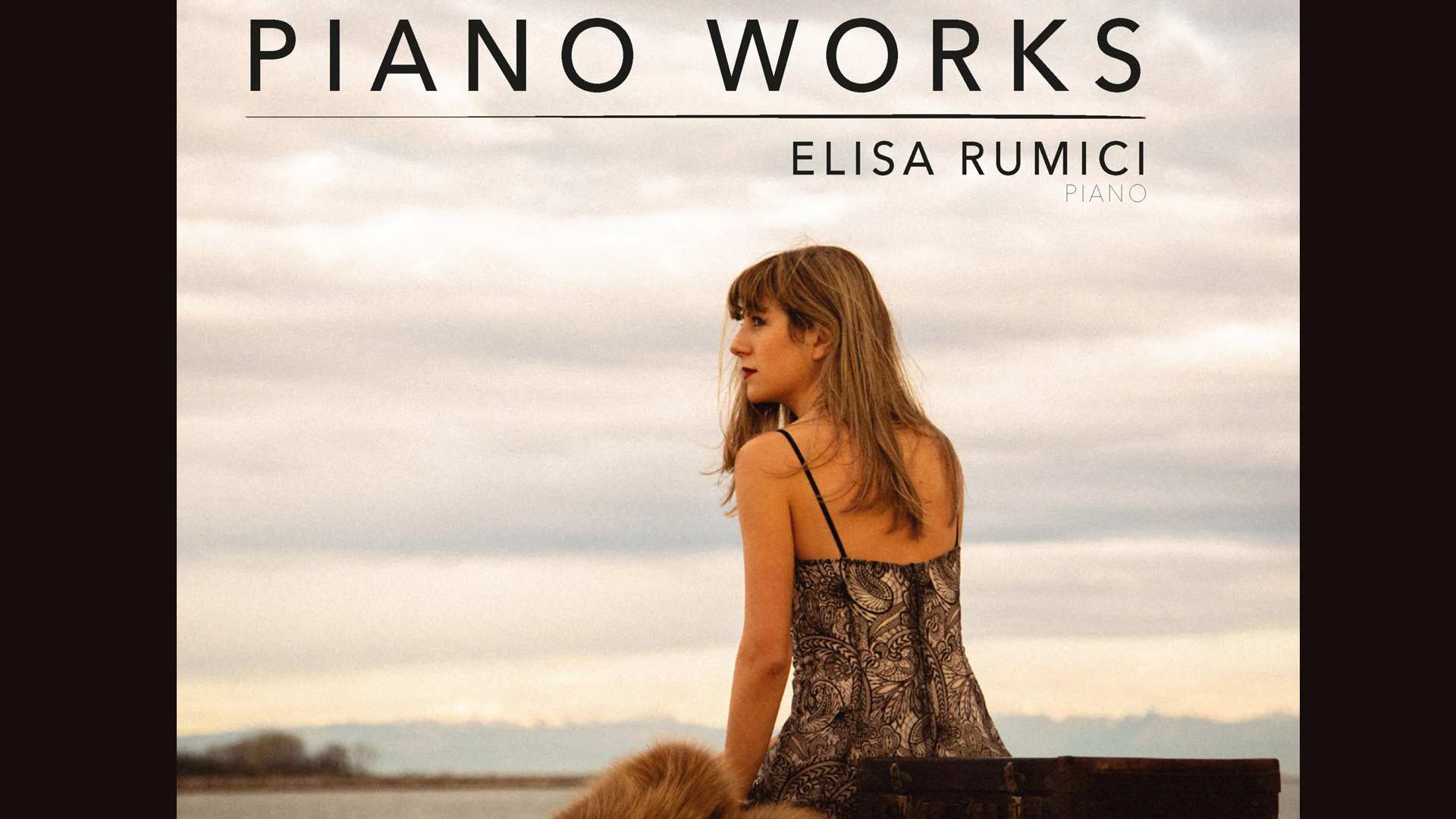 Elisa Rumici sitzt auf einem Koffer am Meer und schaut in die Ferne