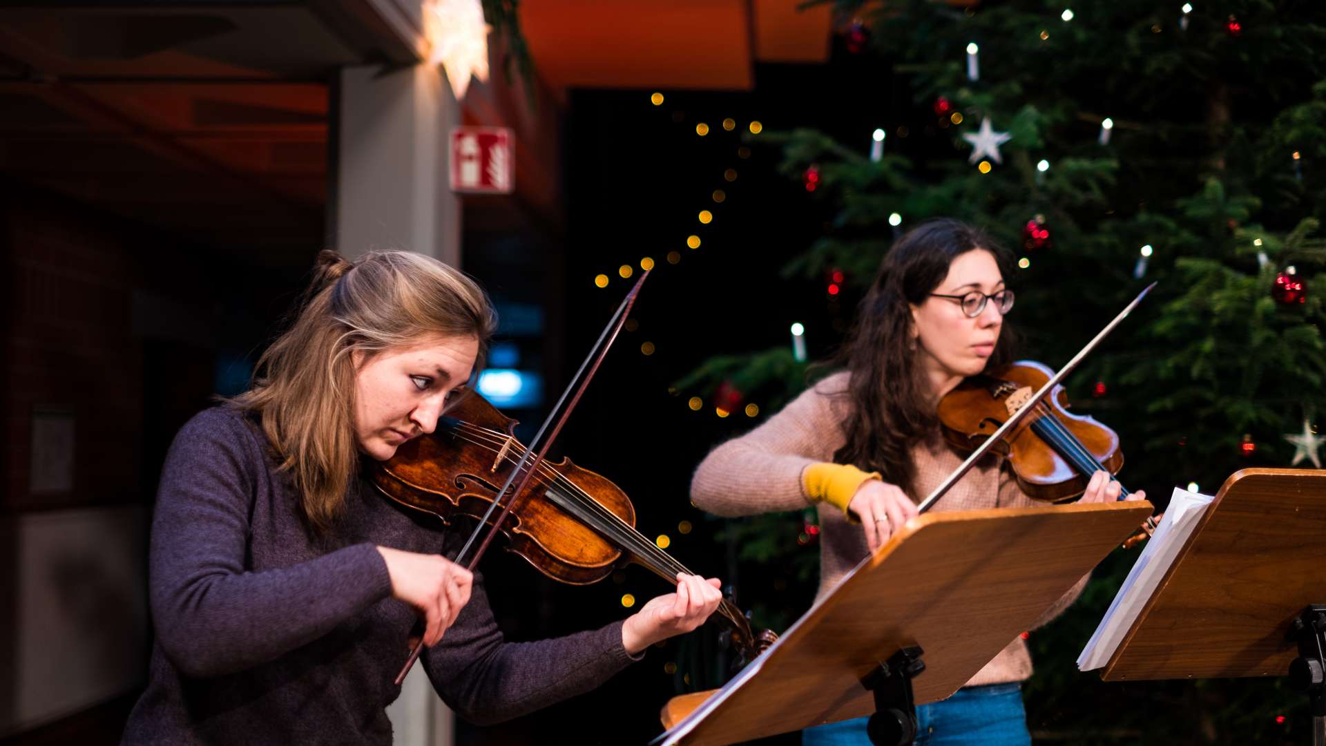 Zwei Studentinnen spielen Geige vor dem Weihnachtsbaum im Foyer der Hochschule