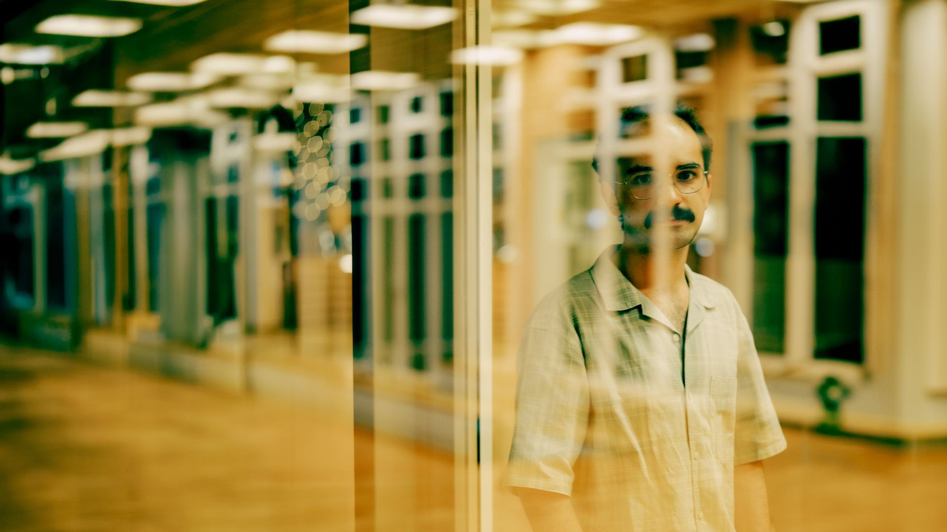 Gespiegelte Fensterfront des Foyers vor dem Kammermusiksaal mit dem Komponisten İlyas Güneş im Halbportrait