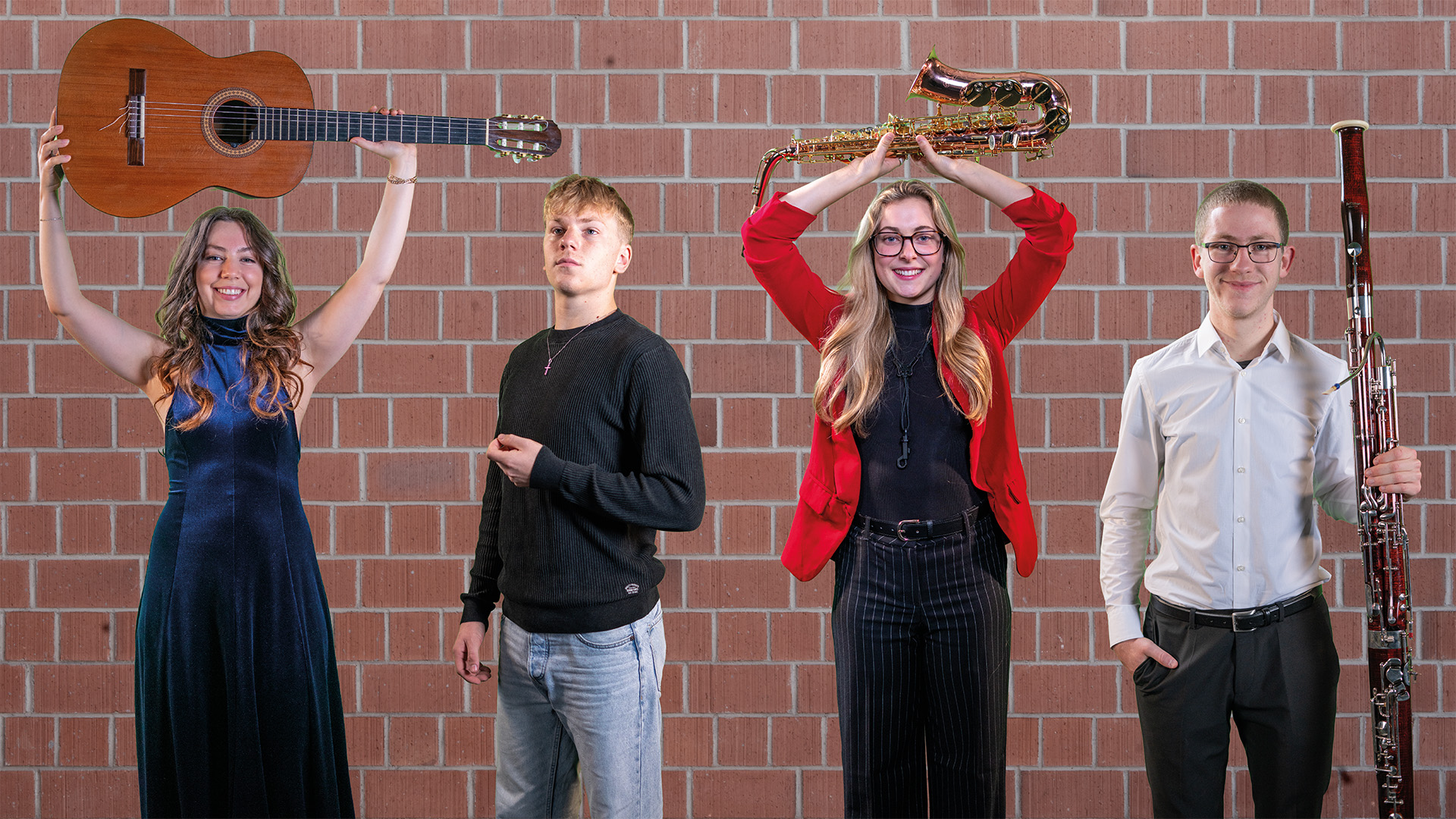 Vier Studierende stehen mit ihren Instrumenten vor einer Ziegelwand