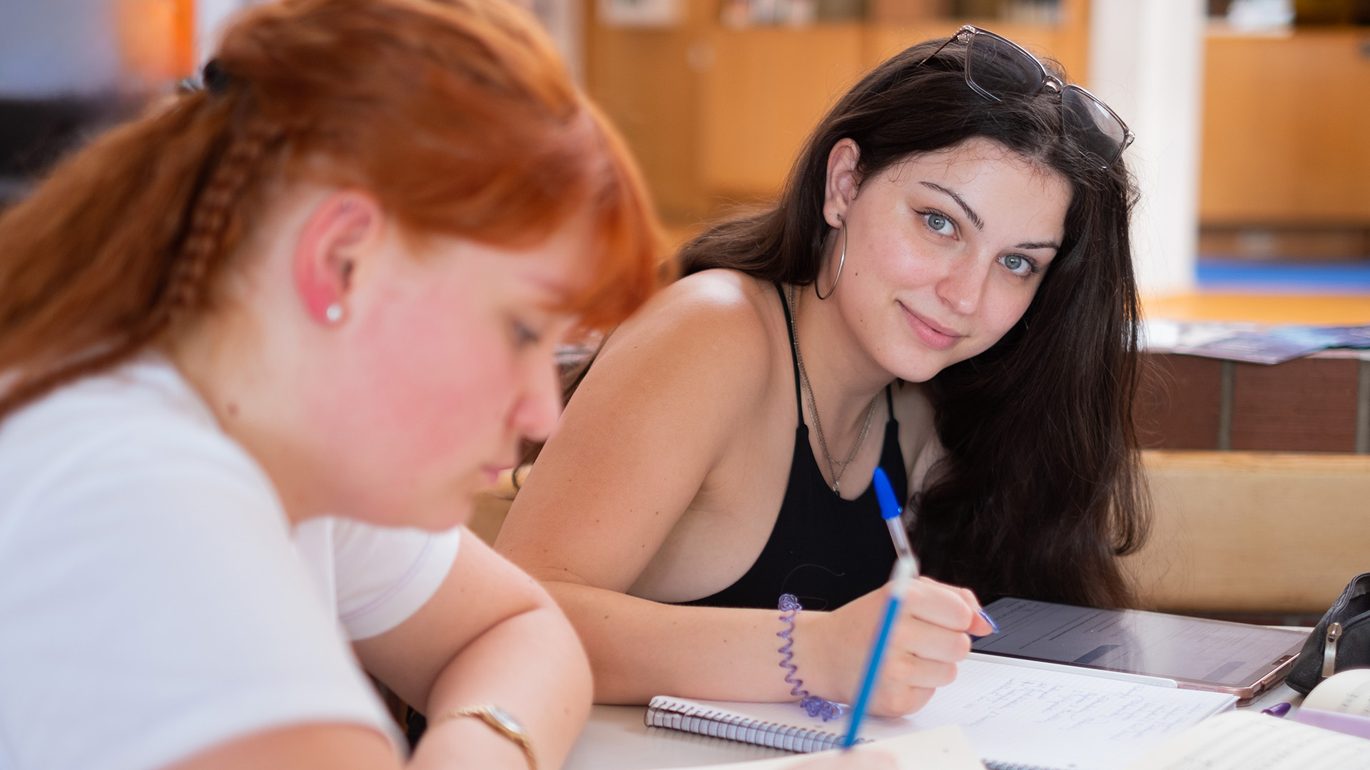 Zwei junge Frauen sitzen schreibend an einem Tisch.