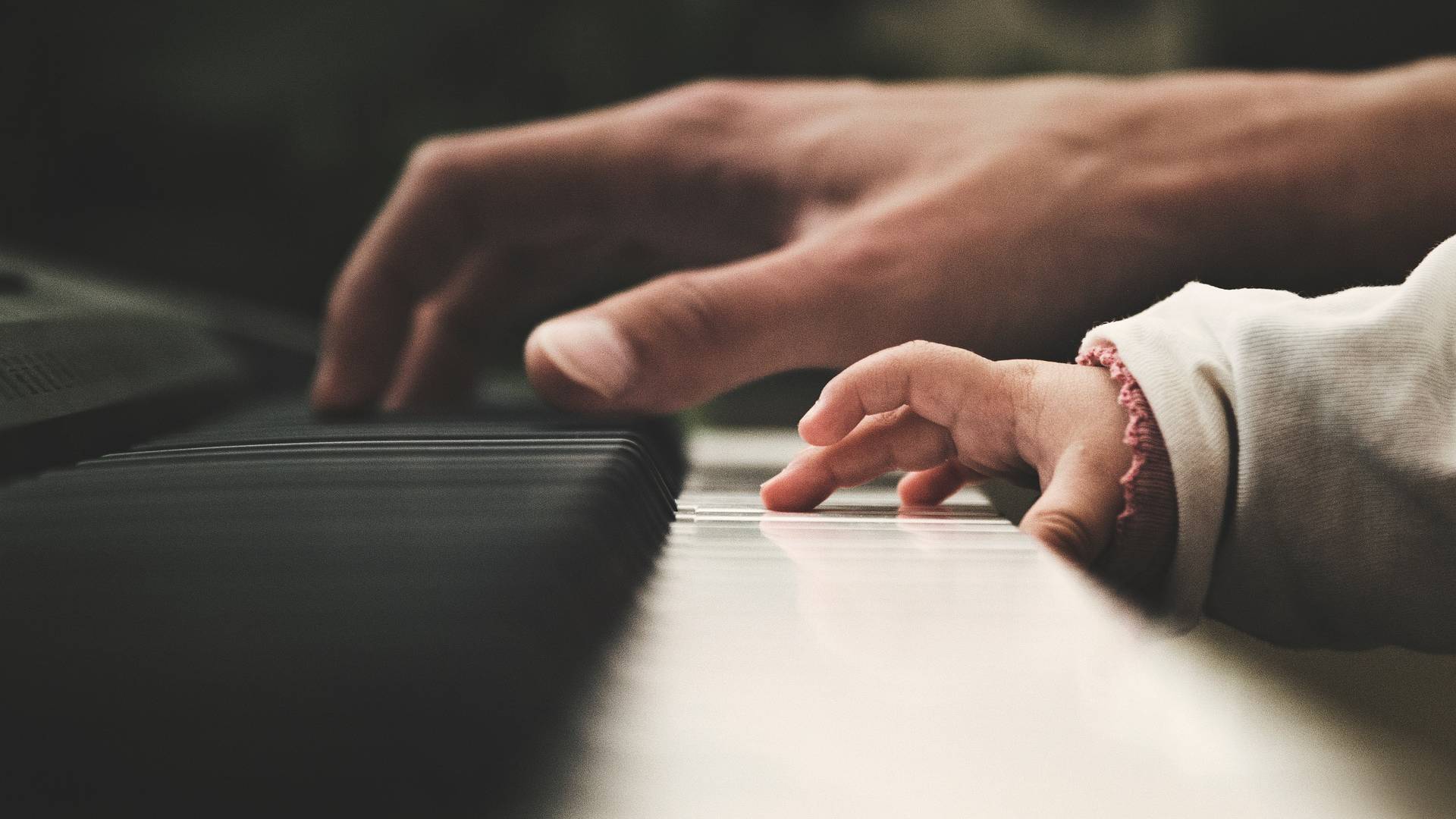 Eine Babyhand neben einer Erwachsenhand auf Klaviertasten