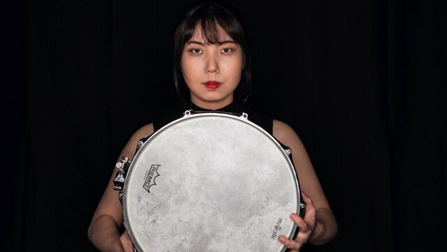 Schlagzeugerin mit einer hellen Rahmentrommel in der Hand vor einem schwarzen Hintergrund