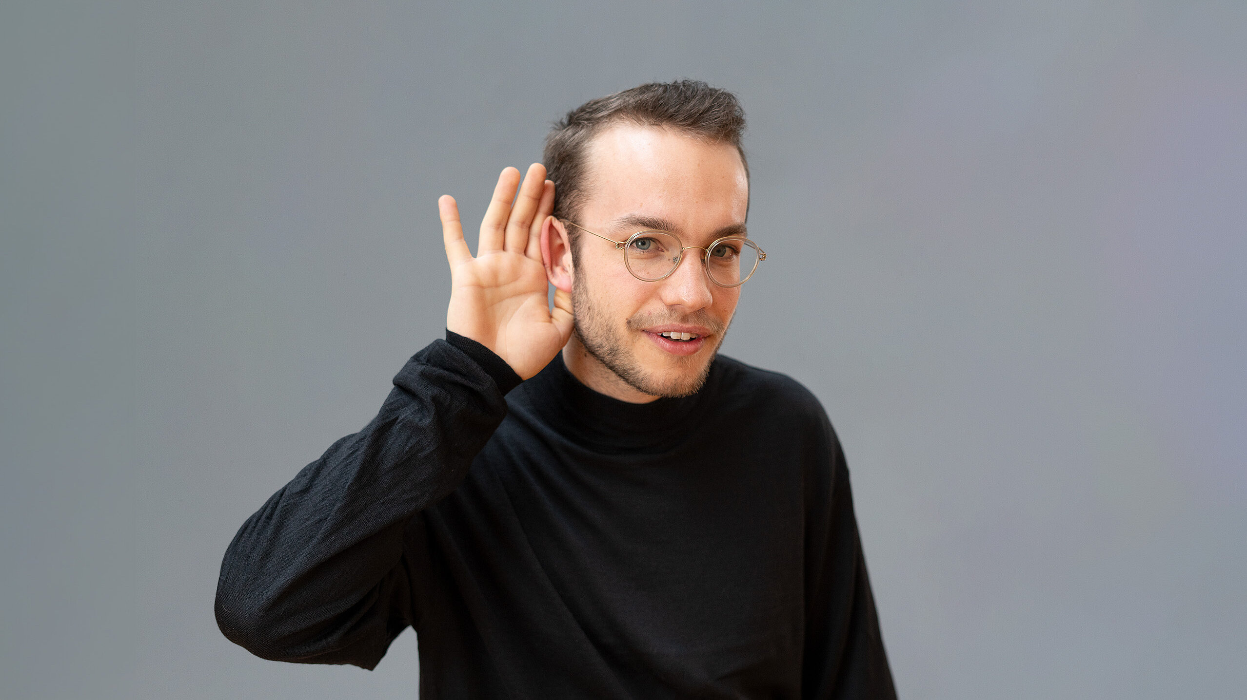 Ein junger Mann hält die Hand ans Ohr und horcht