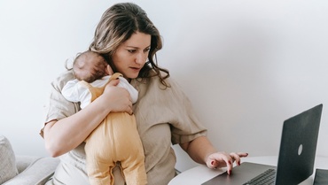 Eine Mutter mit Kind im Arm am Laptop