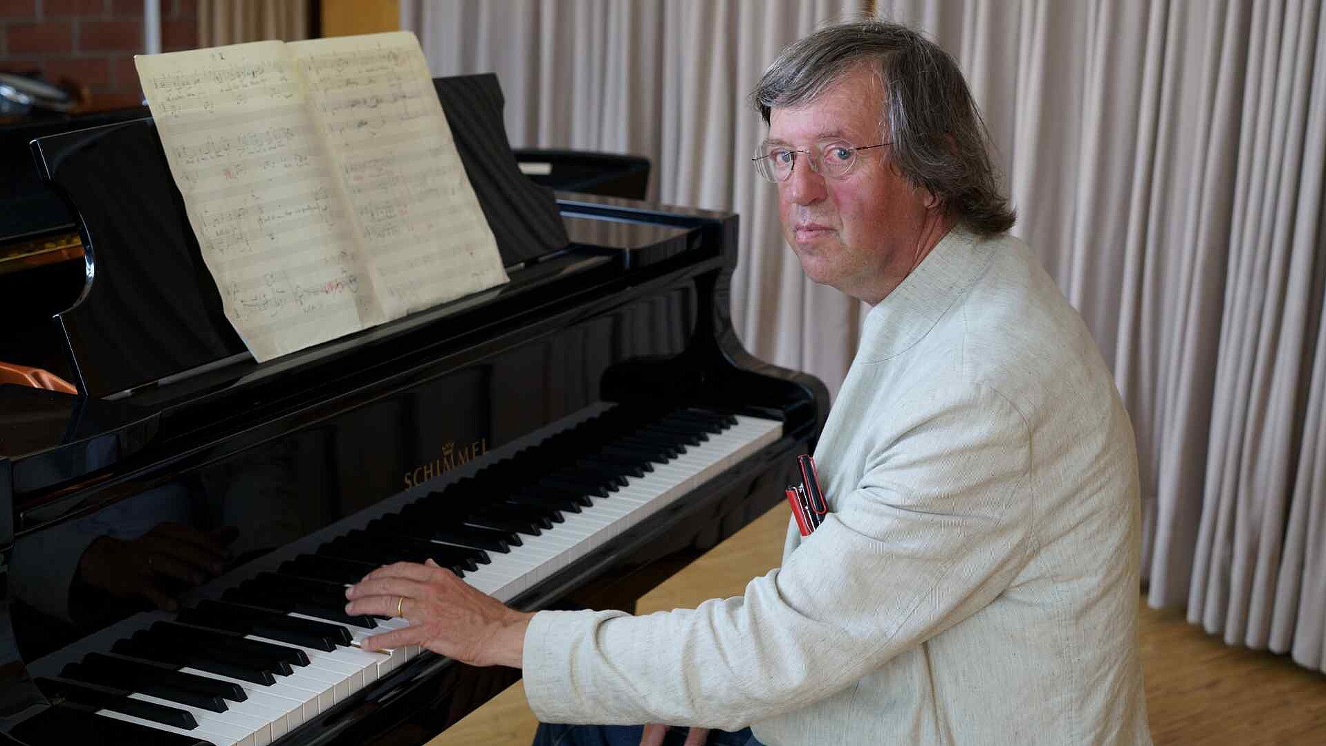 Otfried Büsing in einer weißen Jacke spielt an einem schwarzen Flügel