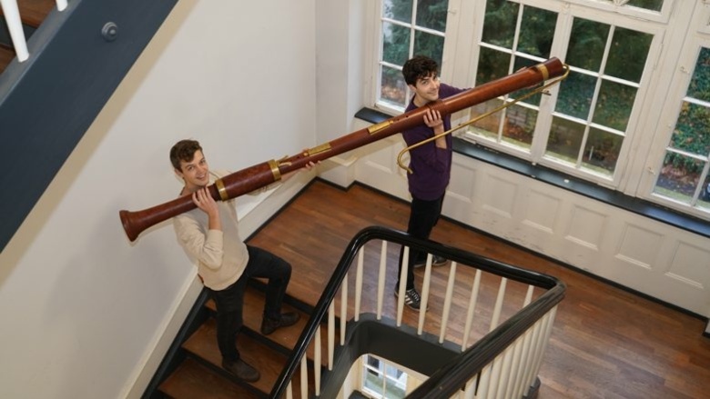 Zwei Studenten tragen die Riesen-Blockflöte durch ein Treppenhaus