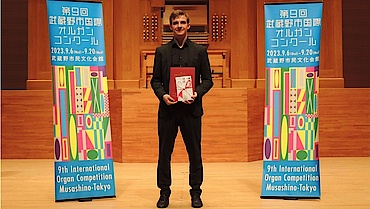 Niklas Jahn steht vor einer Orgel zwischen zwei Bannern