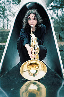 Laura Ferreira kniet auf einem Spielplatz auf einer Rutsche, in der Hand hält sie ein Horn