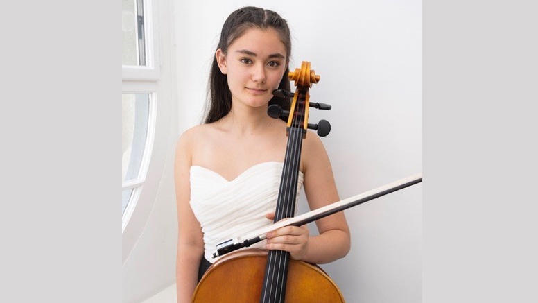 Yuna Dierstein steht mit einem Cello in der Hand vor einer Wand