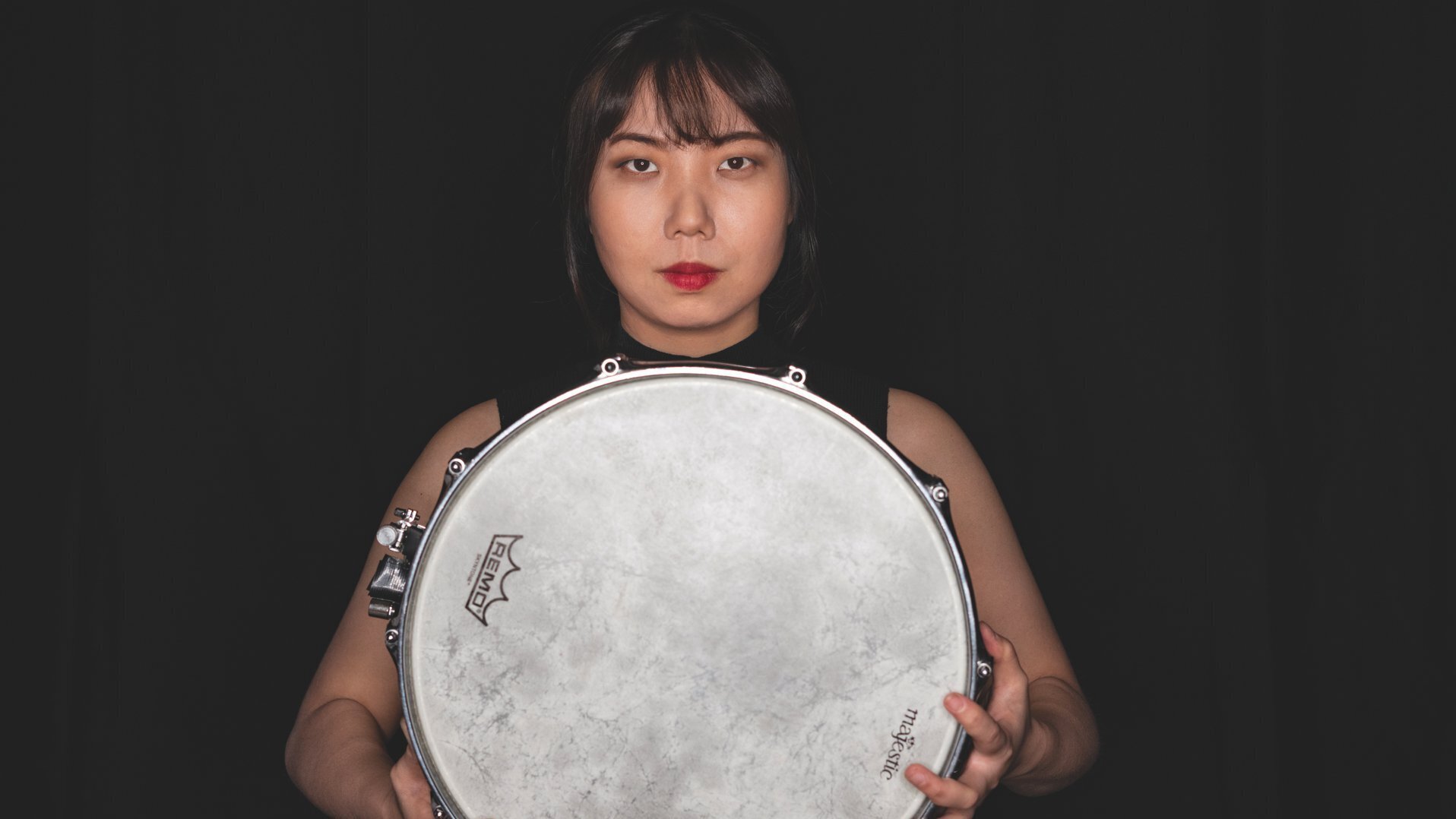 Schlagzeugerin vor schwarzem Hintergrund hält eine Rahmentrommel vor sich