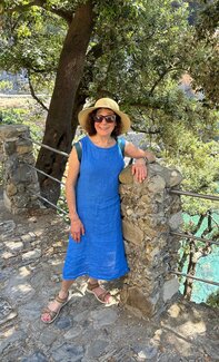 Stephanie Baer steht in einem blauen Kleid mit Strohhut auf dem Kopf vor einem Baum