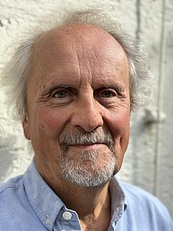 Porträt von Wolfgang Motz in einem hellblauen Hemd vor einer hellen Wand