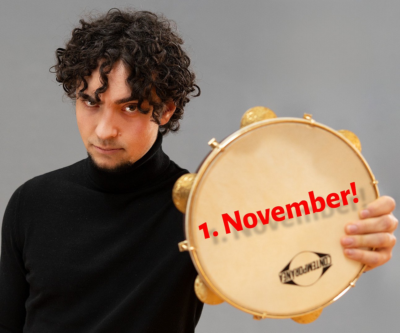 A drummer holds up a tambourine to the camera; it says “November 1!”