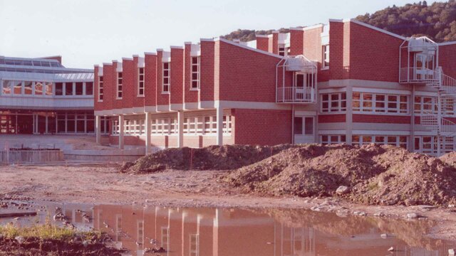 Die neue Hochschule im Bau mit Erdhügeln vor dem Gebäude