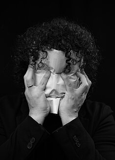 Maximiliano Soto Mayorga drückt sich ein Blatt mit Notenlinien ins Gesicht, hinter ihm ist es schwarz