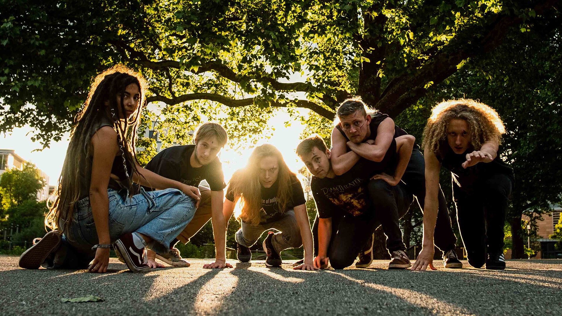 Die sechs Bandmitglieder hocken im Gegenlicht auf einer Straße