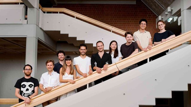 Gruppe von Promovierenden auf einer Treppe im Foyer der Hochschule von unten gesehen