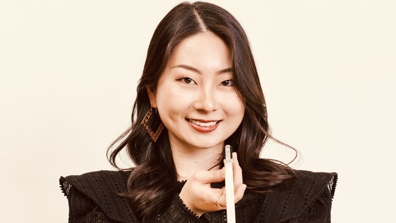 Tomoka Yamagata in einem schwarzen Kleid mit Geigenbogen in der Hand