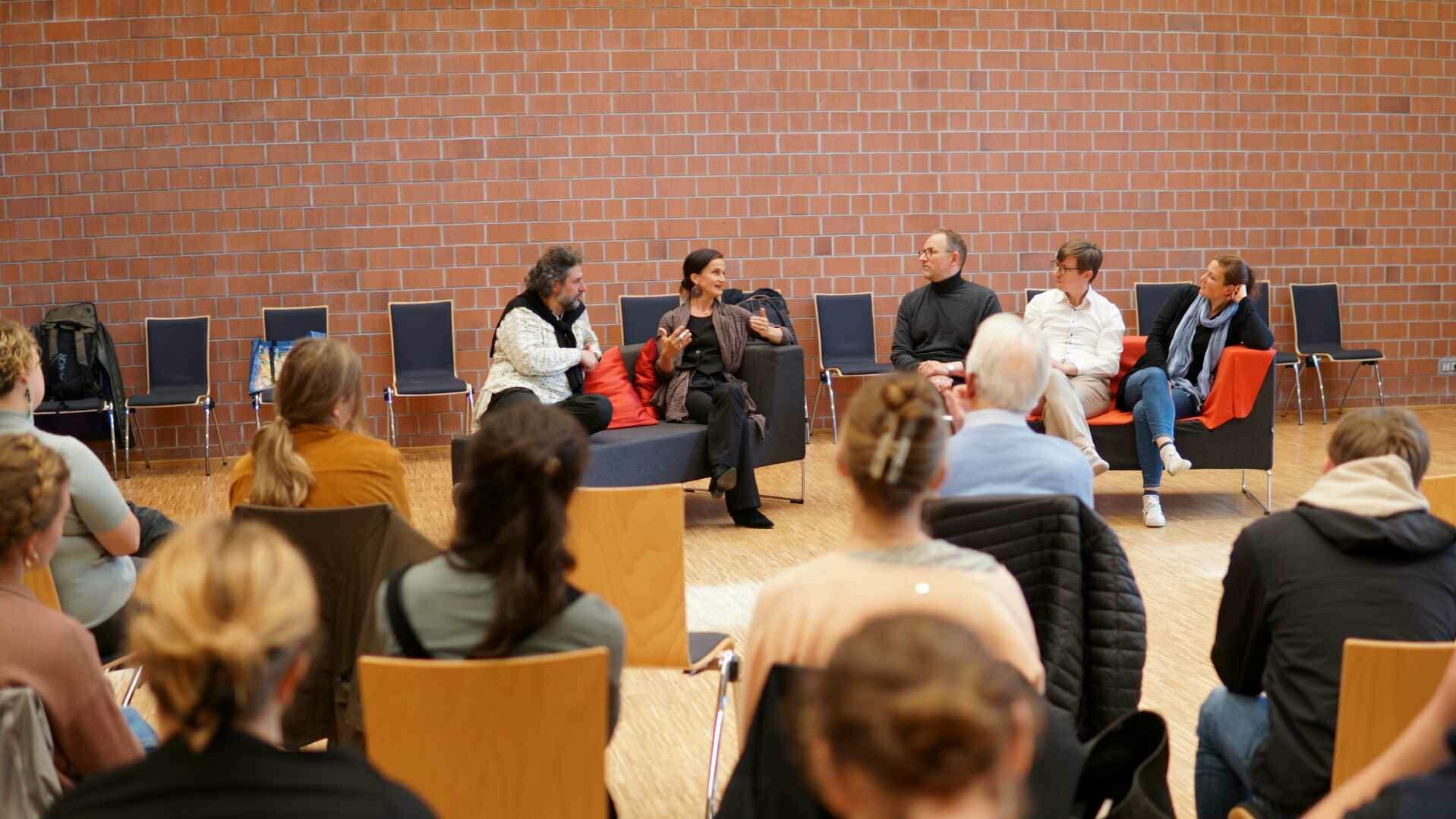 Studierende blicken in die Richtung von vier Sängerinnen und Sänger des RIAS-Kammerchor, die im Rahmen des Projekts Rotes Sofa von Prof. Torsten Meyer interviewt werden.