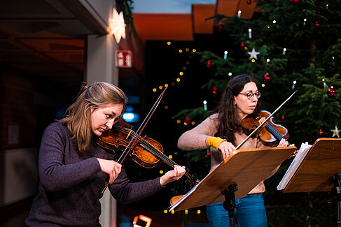 Zwei Studentinnen spielen Geige vor dem Weihnachtsbaum im Foyer der Hochschule