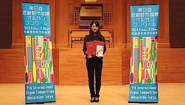 Risa Toho steht vor einer Orgel und zwei Bannern
