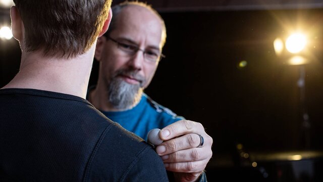 Ein Wissneschaftler der Musikmedizin bringt einen Sensor auf der Schulter eines Musikers an