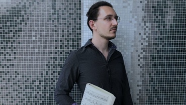 Maurice Florin steht mit Noten in der Hand vor einer gekachelten Wand