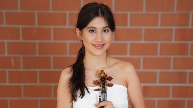 Eine junge Geigerin mit dunklen Haaren und Augen in einem weißen Kleid im Foyer der Hochschule