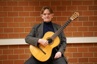 Michael Hampel sitzt mit Gitarre vor einer Backsteinmauer