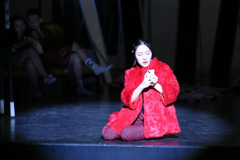 Sängerin in roter Robe sitzt auf dem Boden einer Bühne