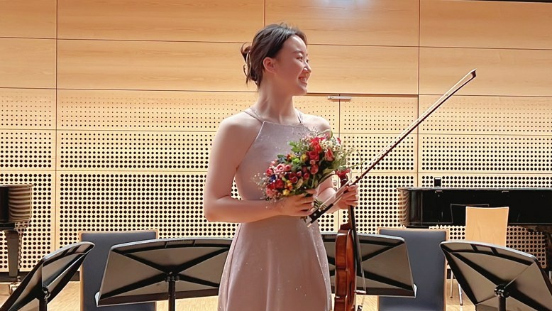 Buwen Lou steht mit Geige in der Hand in einem Konzertsaal