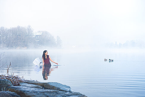 Sophie Hunold steht in einem Nebel-verhangenen See, vor ihr ein Notenständer, neben ihr schwimmen Enten